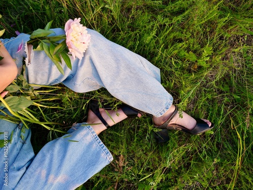 Happy smiling young woman in summer outdoors in a field with pink peony flowers enjoying life in a moment at sunset