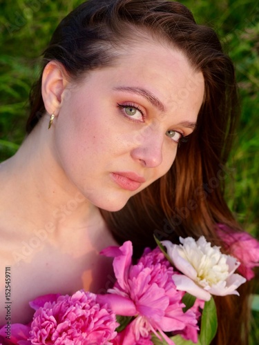 Happy smiling young woman in summer outdoors in a field with pink peony flowers enjoying life in a moment at sunset