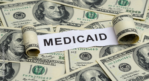Medicaid concept with rolled up hundred dollar bills and paper cutout on currency background view from above