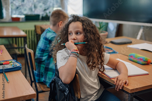 Fotografi Elementary school student chewing on pencil while thinking in classroom