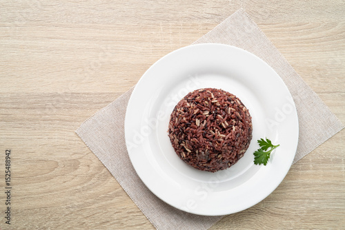 Cooked brown rice or riceberry rice on white plate on wood table
