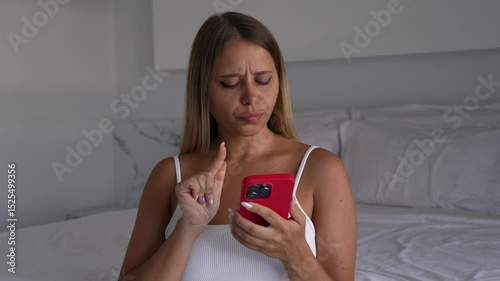 A young blonde woman holding mobile phone hesitates before sending an emotional message, then gathers courage, taps the screen and quickly puts the phone aside. Vulnerability, courage moment