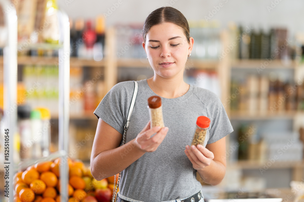 Fototapeta premium Young woman buyer chooses seasoning herbs in jar in grocery store