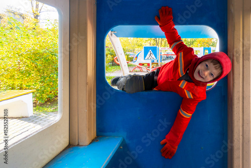 Child with red raincoat of firefighter clings to a rope in a playground during rain. High quality photo