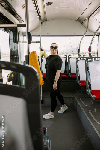 A confident woman in a black outfit standing near the entrance of a modern city bus. Great for illustrating smart commuting, urban lifestyle, public transport, and independent travel.