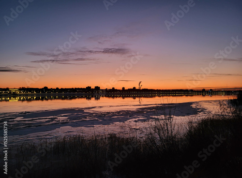 The outline of the city against the background of a pink sunset over a winter river