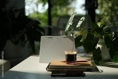 Coffee glass cup and notebook on white table under morning sunlight