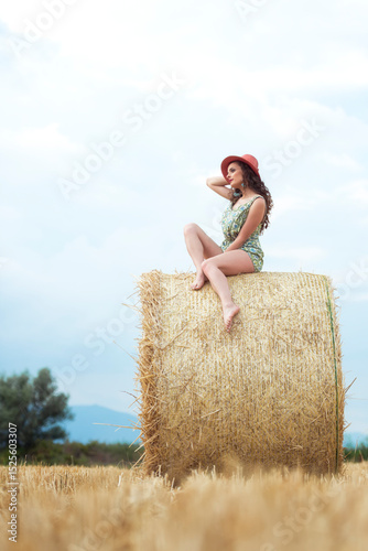 Woman on hay bale with upward gaze and confident posture in rural setting