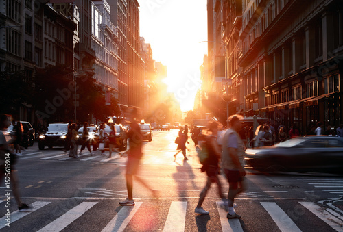 Busy intersection with people and cars in motion on 5th Avenue and 23rd Street in New York City with sunlight background