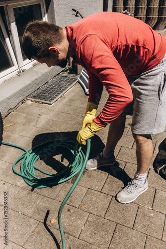 Man winding green garden hose preparing for watering plants outdoors summer gardening tool nature care photo