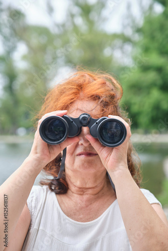 Senior Hispanic woman using binoculars, portrait looking at camera. Concept: The wellbeing of maintaining an active lifestyle in contact with nature.