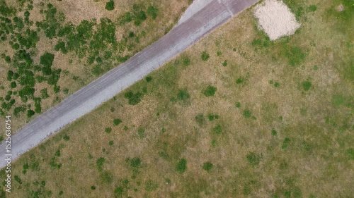 Aerial view of a triangular building near a beach, surrounded by grass, a road with parked cars, and walking paths leading to the shoreline.