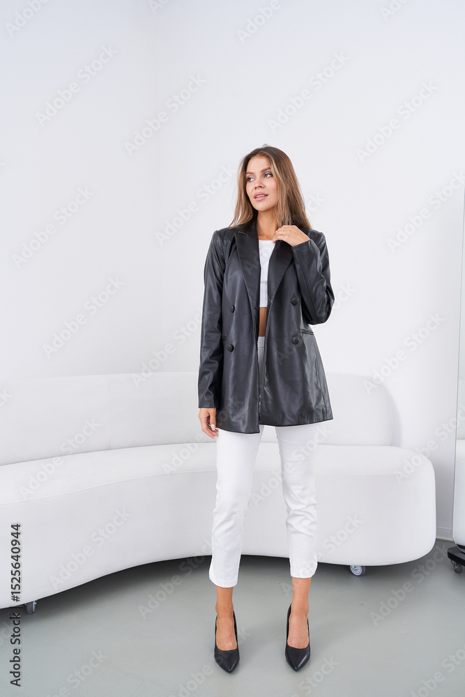 custom made wallpaper toronto digitalStylish woman in a black jacket, white top, and pants, standing by a modern white sofa. She wears black heels and has long brown hair, with a confident expression and casual stance