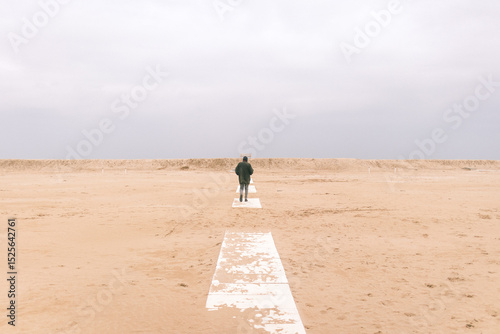 Persona sola vicino a una panchina sulla duna sotto cielo grigio..