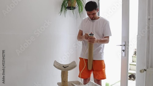 One man is repairing a cat's house by tearing off an old jute thread.