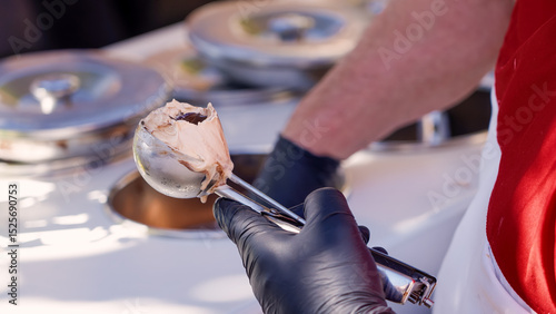 Ice cream vendor with black gloves using a metal scoop to serve the traditional Tartufo dessert in Pizzo, Italy