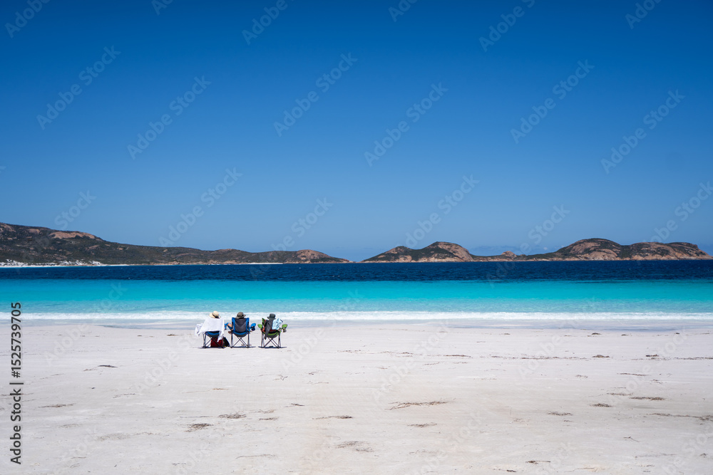 Obraz premium Three people relaxing on beach chairs facing turquoise ocean view