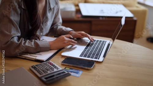Close-up view of Asian woman typing on laptop keyboard, surrounded by finance tools and credit cards