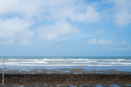 Quiet Beach with Gentle Surf and Pebble Ground Under Clouds: A peaceful image of a beach featuring pebbles and sand, where soft waves meet the shore under a sky with varying cloud cover.