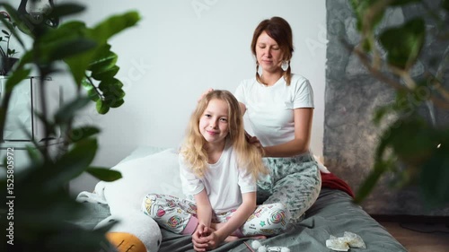 Morning hair care moment as mom combs daughters hair while smiling. Everyday life full of love, connection and gentle parenting at home.