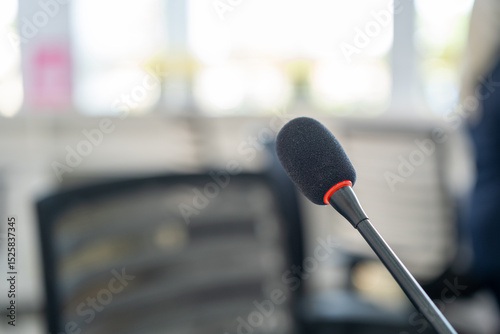 Close-up of a black gooseneck microphone with red accent in a modern office setting, used for communication or public address systems.