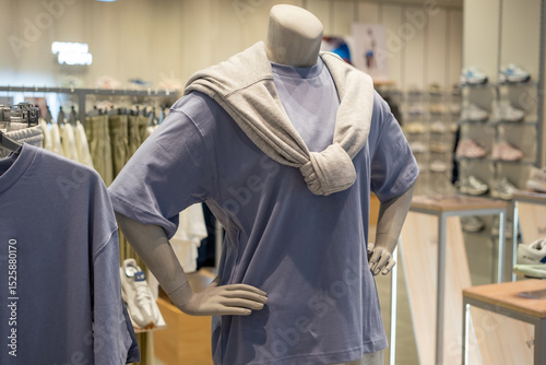 Mannequin dressed in a purple t-shirt with a beige sweatshirt tied around the shoulders, displayed in a modern clothing store.