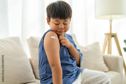 Portrait of happy smile vaccinated little asian kid boy children ages 5 to 11 years old posing show arm with medical plaster after Injection vaccine Covid-19 protection.coronavirus vaccination kid