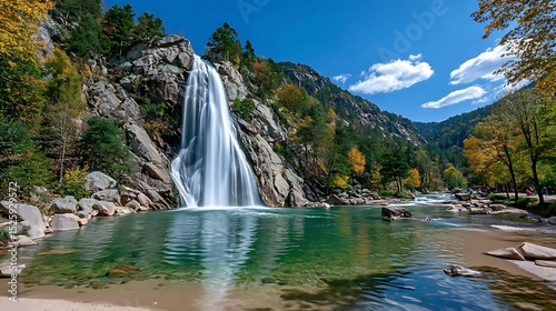 Majestic Waterfall Cascading into Clear Green Pool Surrounded by Lush Trees and Mountains