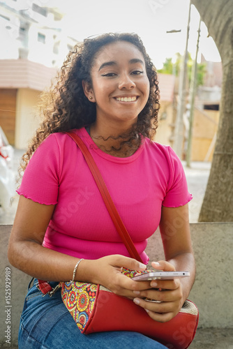Young latin american woman using mobile phone and smiling outdoors