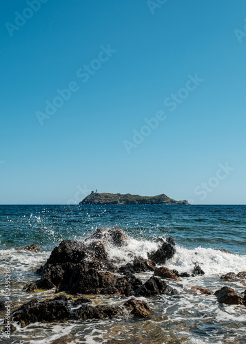 Waves splashing onto the rocky coastline of the northern tip of Cap Corse on the Mediterranean island of  Corsica with the island of Giraglia in the distance