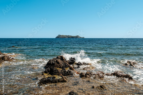 Waves splashing onto the rocky coastline of the northern tip of Cap Corse on the Mediterranean island of  Corsica with the island of Giraglia in the distance