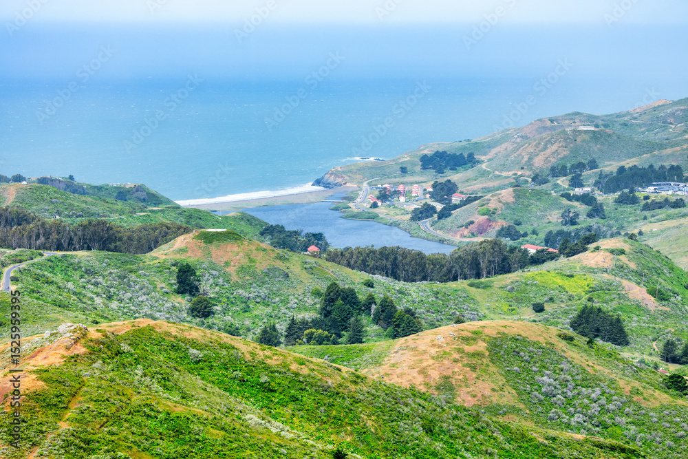 Fototapeta premium Scenic panoramic view of Marin Headlands with winding road, lush green hills, and Pacific Ocean coastline on a clear spring day, California nature landscape