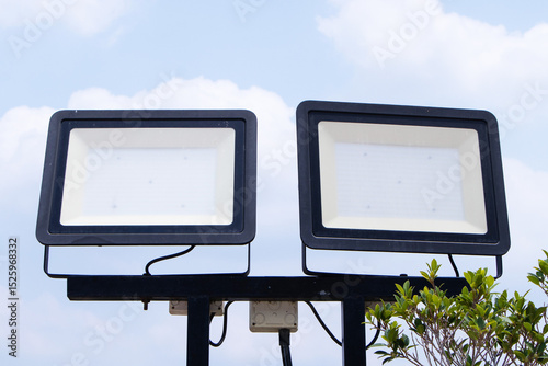 LED spotlight small white sky, cloud in background. Technology that provides light electric in wide area. Shaped set in park to illuminate night. Safety floodlight on roads.