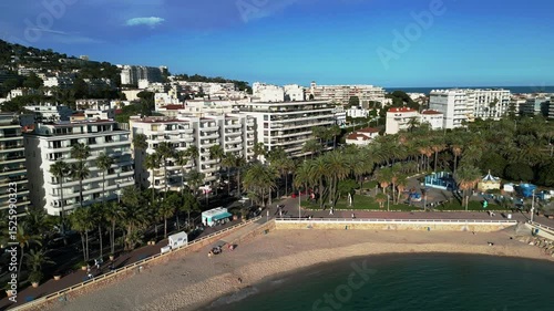 Aerial view of the azure coastline and cityscape of Cannes, France. The scene includes sandy beaches, palm trees, and modern buildings along the shore. Website backgrounds, YouTube vlogs, relaxation photo