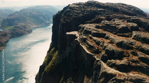 Grandeur of Lysefjord dominated by imposing Preikestolen. Steep face of cliff towering over deep blue fjord with hints of distant peaks in Norway