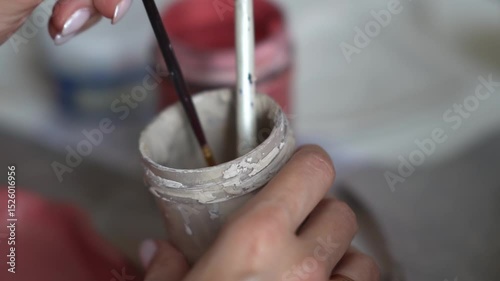 Cropped woman's hands prepare a clay blank. A woman paints clay pottery. A girl dips a brush into a can of paint. Creative handicraft production of tableware
