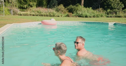Mature couple relaxing in pool, enjoying drinks and sunshine together