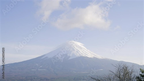 Mount Fuji stands tall with a snow-covered summit against a clear blue sky. The surrounding landscape showcases vibrant spring foliage