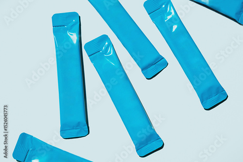Blue Foil Sachets are Scattered on Light Blue Background. Packaging for Single Serving Products. Food and Beverage Industry.