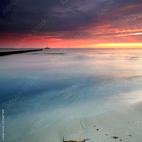 Whispers of the Sea: Vibrant Sunset Casting Golden red Light on Weathered Wooden Groynes
