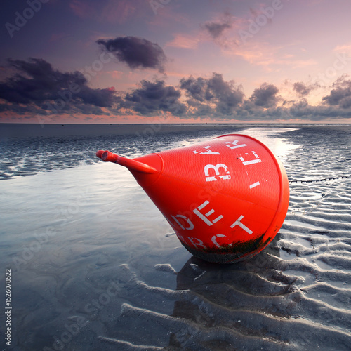 Sunset Sentinel: Weathered Orange Buoy Resting on Sandy Shores
