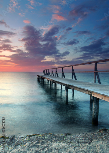 beautiful Vibrant Sunset Casting red Light on Weathered Wooden pier over the sea