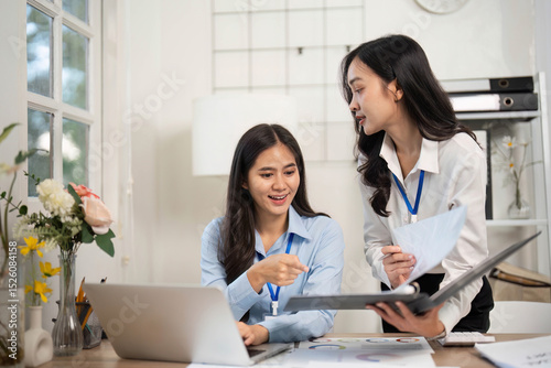Collaborative Office Environment. Two women discussing project insights at a desk.