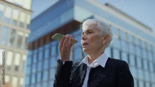 Senior woman using voice assistant on smartphone outdoors