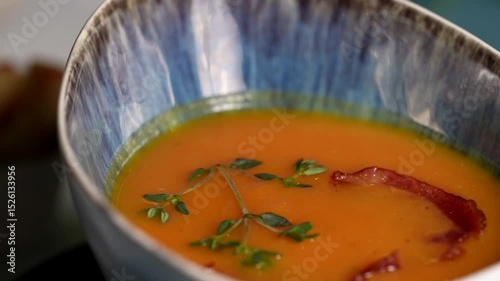 Close-up of tomato cream soup with herbs and crispy bacon, presented in a blue patterned ceramic bowl.