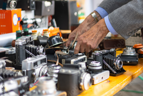 Close-up of a variety of vintage cameras on a flea market with the hands of and old man grabbing one of them