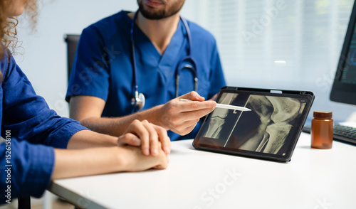 Cuadro en lienzo Doctor consults patient and explains knee x-ray results using tablet in clinic