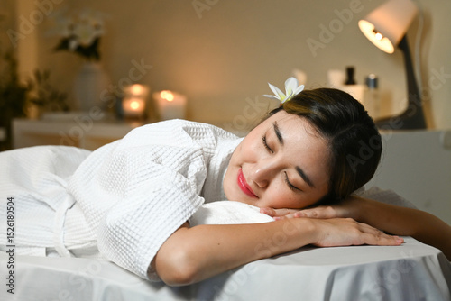 A woman is laying on a massage table with a white robe on. She is smiling and she is relaxed