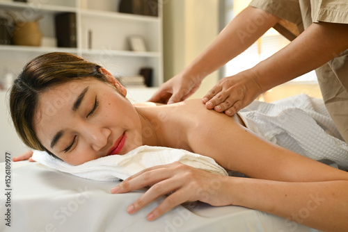 A woman is getting a massage from a massage therapist. She is smiling and relaxed. The massage table is covered with a white towel