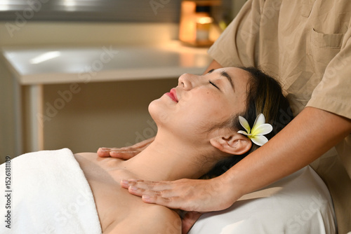 A woman is lying on a massage bed and a masseuse is massaging her shoulders. The atmosphere is relaxing and peaceful.